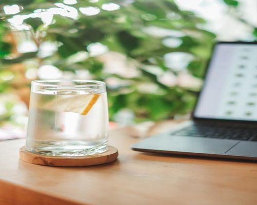 A modern working lifestyle scene showing a well organized desk with a clear glass of water and a portion of fresh sliced avocado